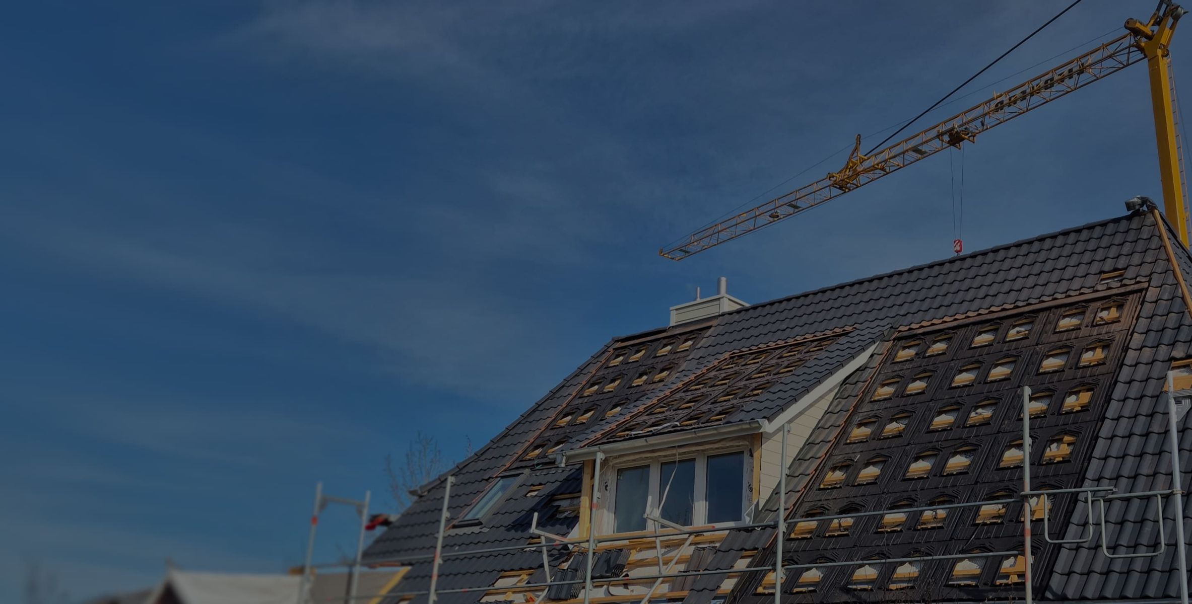 Neubau mit Kran und Handwerkern bei Dacheindeckung vor blauem Himmel
